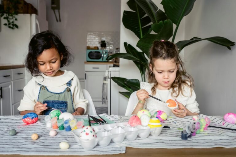 Two children painting colorful Easter eggs at a kitchen table.